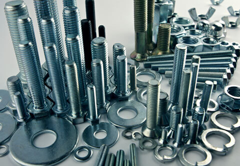 A variety of metal fasteners, including screws, bolts, nuts, and washers, are arranged in a scattered manner on a flat surface