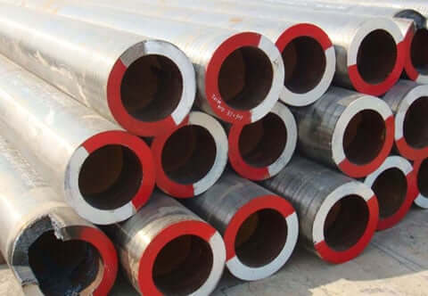 A pile of large metal pipes with red inner rims is stacked together