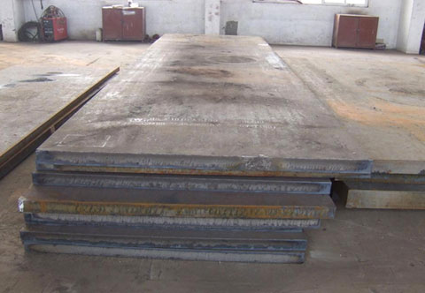A stack of large, rectangular metal sheets lies on the floor of an industrial workshop