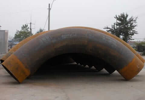 A stack of large, rusted, curved metal pipes are arranged on a concrete surface