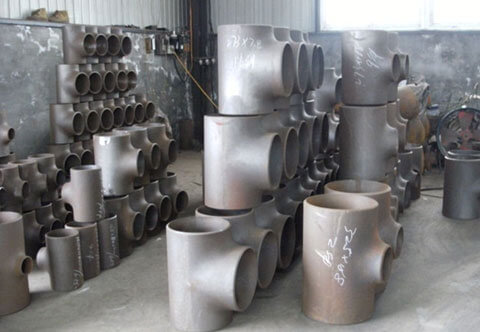 The image shows a workshop with piles of metal pipe fittings, including tees and elbows, stacked on the floor and on shelves