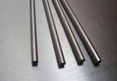Four long, cylindrical metal rods are placed parallel to each other on a smooth, reflective metallic surface