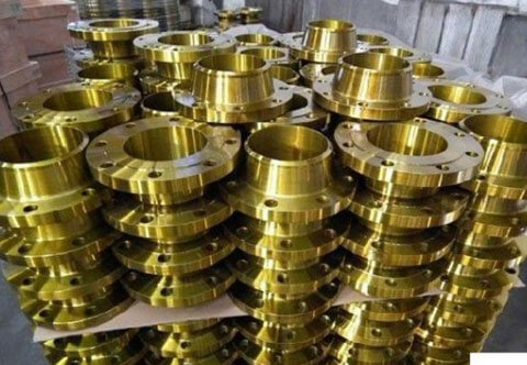 A large stack of shiny, golden metallic flanges are neatly arranged in a warehouse-type setting