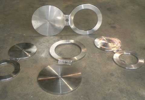 A set of metallic spectacle blind flanges and flat disk plates are laid out on a concrete floor.