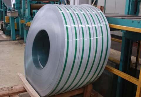 A large coil of sheet metal banded with several green straps is standing on a wooden pallet in an industrial setting
