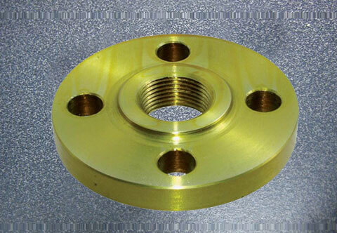 A brass flange with a central threaded hole and four evenly spaced smaller holes around it is placed against a textured gray background